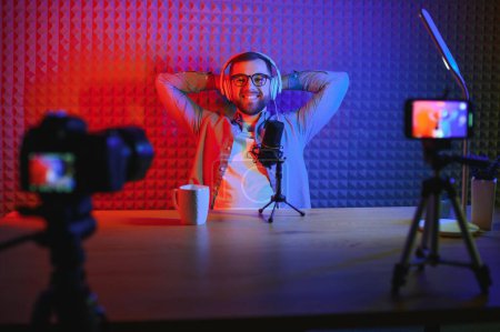 Young man recording or streaming podcast using microphone at his small broadcast studio. Content creator