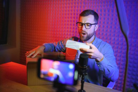 Téléchargez les photos : Joyeux jeune homme enregistrement vidéo de déboxe en studio. - en image libre de droit