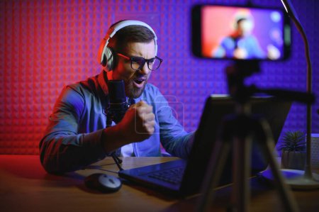 Photo for Streamer is streaming online content,metaverse ar vr,gaming and esports concept.Happy man gamer wear headphone competition video game online with Laptop computer in colorful neon lights - Royalty Free Image