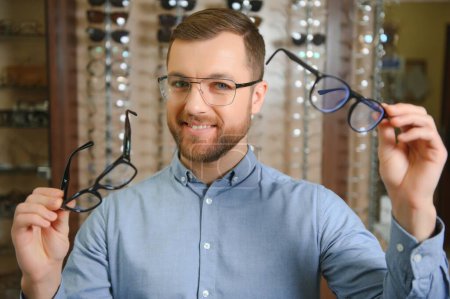 Photo for Big choice. Stylish man with beard choosing glasses in the optics store - Royalty Free Image