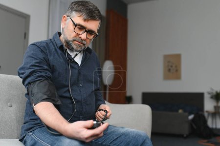 Téléchargez les photos : Homme âgé utilisant un dispositif médical pour mesurer la pression artérielle. - en image libre de droit