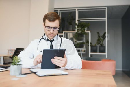 Téléchargez les photos : Male doctor using tablet computer at his office. General practitioner using digital tablet at his clinic - en image libre de droit