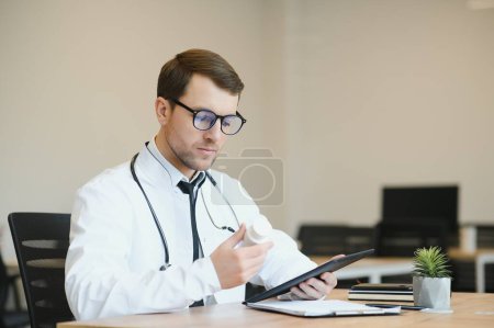 Téléchargez les photos : Médecin masculin utilisant un ordinateur tablette à son bureau. Médecin généraliste utilisant une tablette numérique dans sa clinique - en image libre de droit