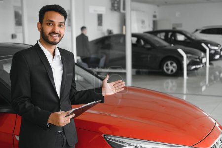 Buen aspecto, alegre y amable vendedor indio posa en un salón de coches o sala de exposición