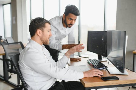 Two men traders sitting at desk at office together looking at data analysis discussing brainstorming successful strategy inspired teamwork concept close-up.