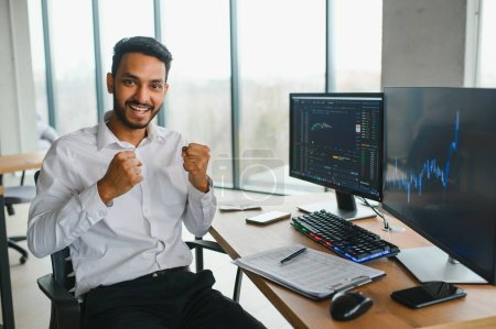 Joven comerciante indio hombre de negocios mirando a la pantalla de la computadora con gráficos comerciales que reflejan en gafas viendo el mercado de valores concepto de crecimiento de datos financieros, de cerca