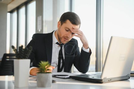 Depressed young businessman holding head in hands, has problem, a laptop on the desk. A guy made a mistake in a work.
