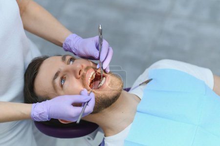 Photo for Young bearded man sitting in dental chair, visiting modern dental clinic, having regular checkup, woman dentist - Royalty Free Image