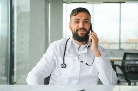 Téléchargez les photos : Jeune 30 ans beau garçon arabe agréable médecin en manteau blanc, posant à la caméra à l'intérieur - en image libre de droit