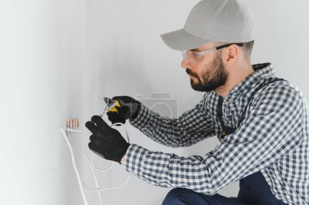Téléchargez les photos : Professional electrician working on a home electrical system, he is installing a wall socket. - en image libre de droit