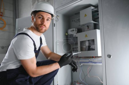 Photo for Man, an electrical technician working in a switchboard with fuses. Installation and connection of electrical equipment. Professional with tools in hand. concept of complex work, space for text - Royalty Free Image