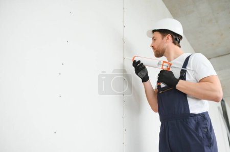 Foto de Trabajador profesional aplicando sellador de silicona con pistola de calafateo en la pared. - Imagen libre de derechos