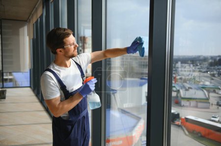 Photo for Male professional cleaning service worker in overalls cleans the windows and shop windows of a store with special equipment - Royalty Free Image