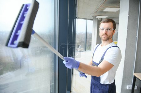 Photo for Male professional cleaning service worker in overalls cleans the windows and shop windows of a store with special equipment - Royalty Free Image