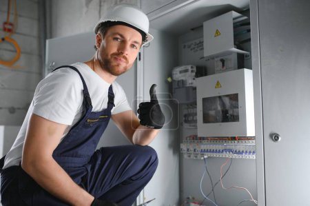 A male electrician works in a switchboard with an electrical connecting cable