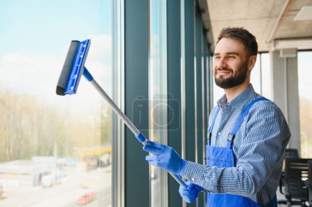 Téléchargez les photos : Homme concierge nettoyage fenêtre dans le bureau
. - en image libre de droit