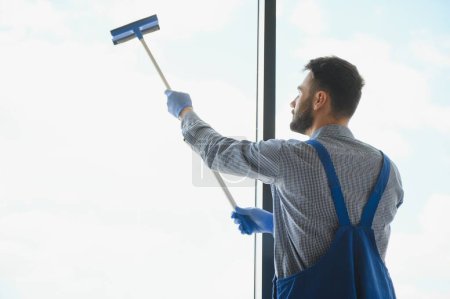 Trabajador de servicio de limpieza profesional masculino en overol limpia las ventanas y escaparates de una tienda con equipo especial.