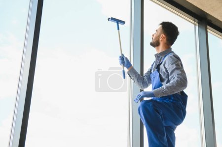 Photo for Male professional cleaning service worker in overalls cleans the windows and shop windows of a store with special equipment. - Royalty Free Image