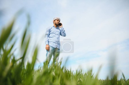 Photo for Portrait of happy young Indian man farmer standing in agriculture land surround by crop holding smartphone talking to someone, smiling village male with mobile phone in field, technology concept. - Royalty Free Image