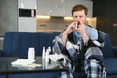 Sick man with nasal spray and paper tissue at home.