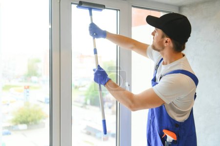 Téléchargez les photos : Homme professionnel de nettoyage travailleur en salopette nettoie les fenêtres - en image libre de droit