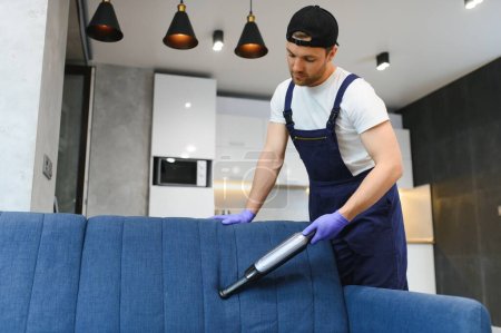 Foto de Professional janitor vacuuming armchair in room, closeup. - Imagen libre de derechos