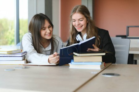 Foto de Dos colegialas de quince años leyendo libros y tomando abstracto en copybooks están haciendo deberes en la biblioteca de la escuela. - Imagen libre de derechos