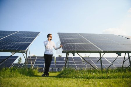 Foto de Hombre de camisa blanca de pie cerca de paneles fotovoltaicos en un día soleado en el campo. - Imagen libre de derechos
