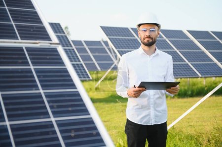 Foto de Inversor masculino barbudo positivo frente a paneles fotovoltaicos que producen energía alternativa - Imagen libre de derechos
