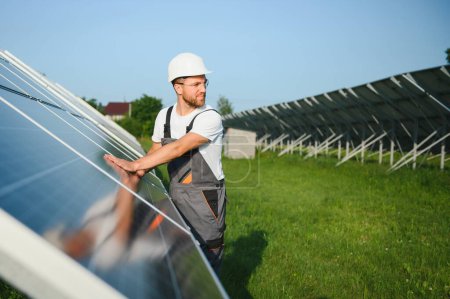 Photo for Side view of male worker installing solar modules and support structures of photovoltaic solar array. Electrician wearing safety helmet while working with solar panel. Concept of sun energy. - Royalty Free Image