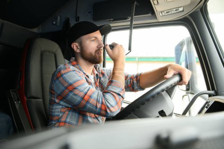 Téléchargez les photos : Homme camionneur conduisant dans une cabine de son camion et parlant sur émetteur radio - en image libre de droit