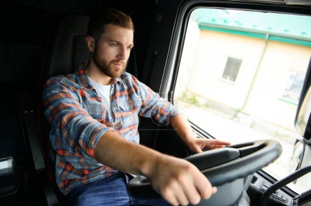 Foto de Vista lateral del conductor profesional detrás del volante en la cabina del camión - Imagen libre de derechos