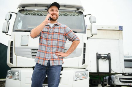 Téléchargez les photos : Chauffeur de camion debout près de son camion et parlant au téléphone. Homme conducteur entrer en contact avec sa famille - en image libre de droit