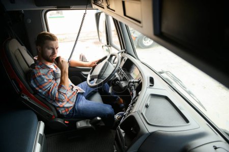 Man trucker driving in a cabin of his truck and talking on radio transmitter