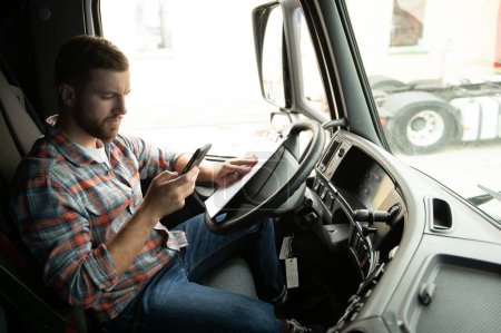 Foto de Joven conductor profesional que se comunica por teléfono móvil mientras conduce un camión - Imagen libre de derechos