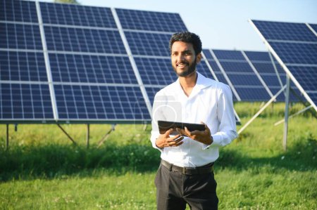 Foto de Ingeniero masculino comprueba una planta fotovoltaica (solar) y utiliza una tableta de grabación. Hombre indio en uniforme celebración tableta - Imagen libre de derechos
