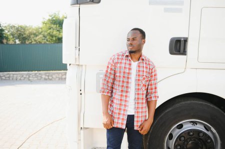 Foto de Vista frontal. Joven camionero africano está con su vehículo durante el día - Imagen libre de derechos
