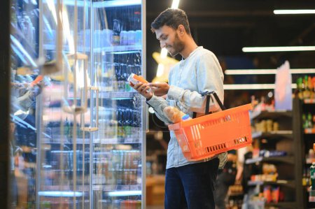 Foto de Retrato de un hombre indio feliz parado frente al mostrador de productos en una tienda de comestibles. Hombre comprar comestibles para el hogar en el supermercado - Imagen libre de derechos