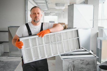 Téléchargez les photos : Un travailleur masculin tient un filtre à air pour la climatisation dans un espace de bureau. Installation d'un climatiseur - en image libre de droit