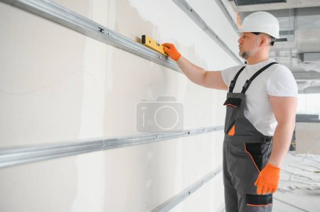 Man holding level against plasterboard, interior drywall. Attic renovation.