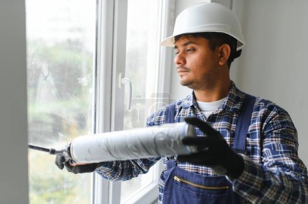 Téléchargez les photos : Travailleur indien utilisant un tube en silicone pour la réparation de la fenêtre intérieure. - en image libre de droit