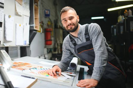 Téléchargez les photos : Homme travaillant dans l'imprimerie avec du papier et des peintures. - en image libre de droit