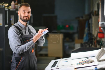 Foto de Trabajador de la casa de impresión que controla la calidad del proceso de impresión y verifica los colores con lupa. - Imagen libre de derechos