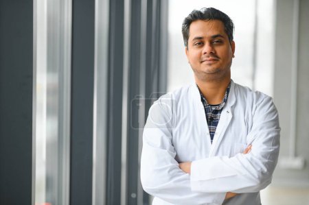 Portrait of male indian doctor on clinic corridor as background