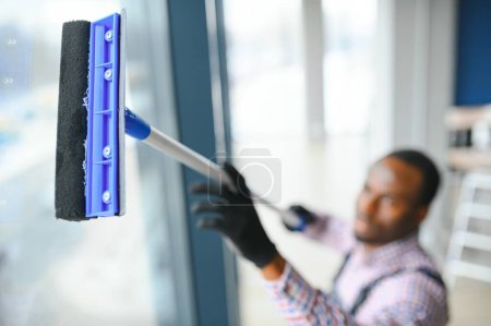 Photo for Happy Male Worker Cleaning Glass With Squeegee And Spray Bottle. - Royalty Free Image