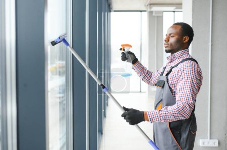 Photo for Happy Male Worker Cleaning Glass With Squeegee And Spray Bottle. - Royalty Free Image