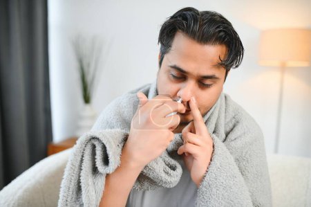 Téléchargez les photos : Rhinite, médecine et concept de soins de santé - homme indien malade en couverture utilisant un spray nasal à la maison
. - en image libre de droit