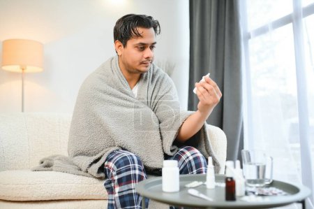 Téléchargez les photos : Rhinite, médecine et concept de soins de santé - homme indien malade en couverture utilisant un spray nasal à la maison
. - en image libre de droit