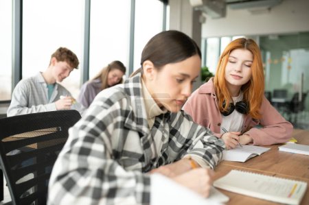 Studenten sitzen am gemeinsamen Schreibtisch und machen sich Notizen über das gemeinsame Lernen an der Universität.