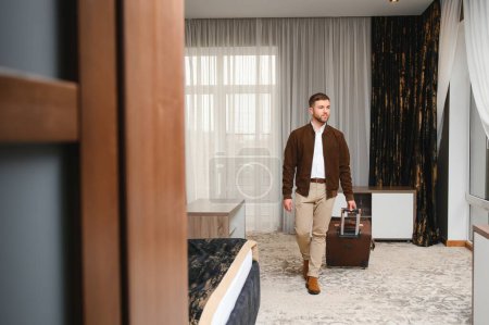 Young businessman with suitcase standing at hotel room. Business trip concept.